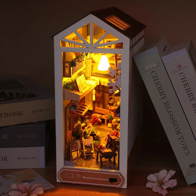 A miniature DIY book nook kit featuring a detailed bookshelf room scene with lighting and decorative elements.
