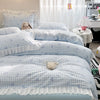 A set of three light blue and white checkered duvet covers with ruffled edges and floral embroidery displayed on a bed.
