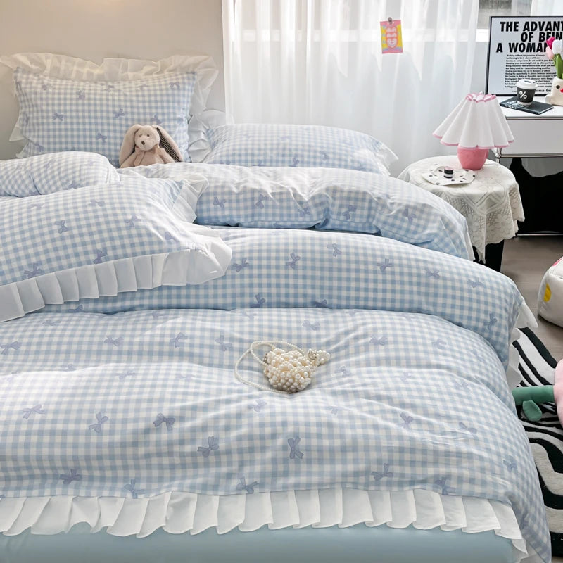 A set of three light blue and white checkered duvet covers with ruffled edges and floral embroidery displayed on a bed.