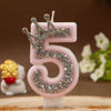 Pink rhinestone crown number candle shaped like the number 5 on a wooden surface.