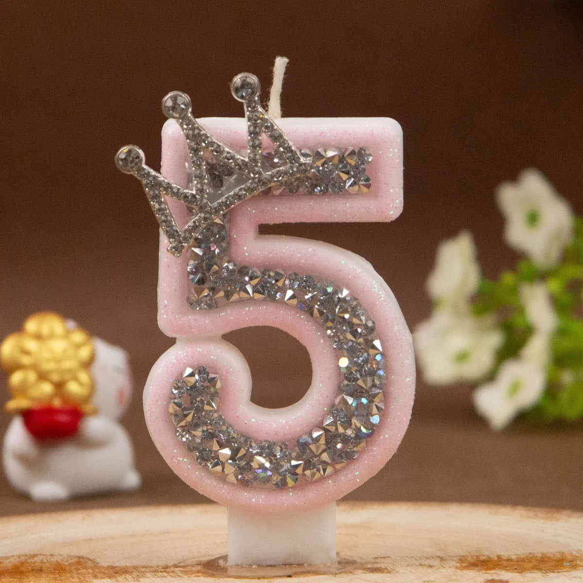 Pink rhinestone crown number candle shaped like the number 5 on a wooden surface.