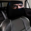 A man wearing a black eye mask is looking over his shoulder while sitting in a gray car headrest.