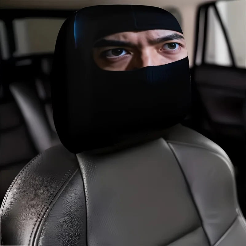 A man wearing a black eye mask is looking over his shoulder while sitting in a gray car headrest.