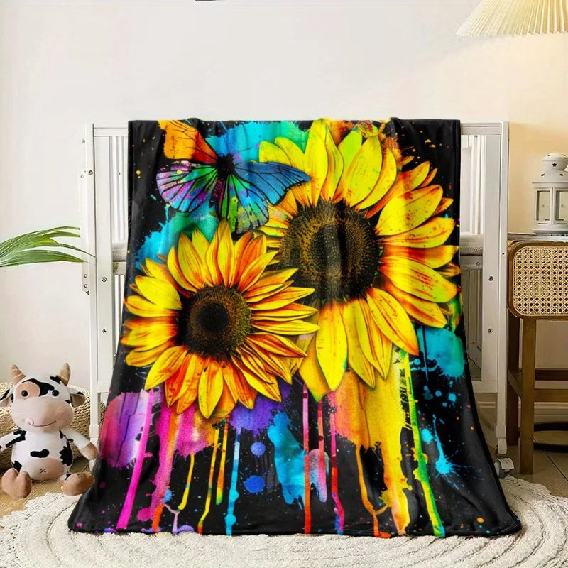 A vibrant floral print blanket featuring large yellow sunflowers and colorful paint splatters on a black background.