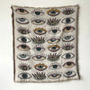 A woven throw blanket featuring a pattern of stylized eyes in various colors and shades.