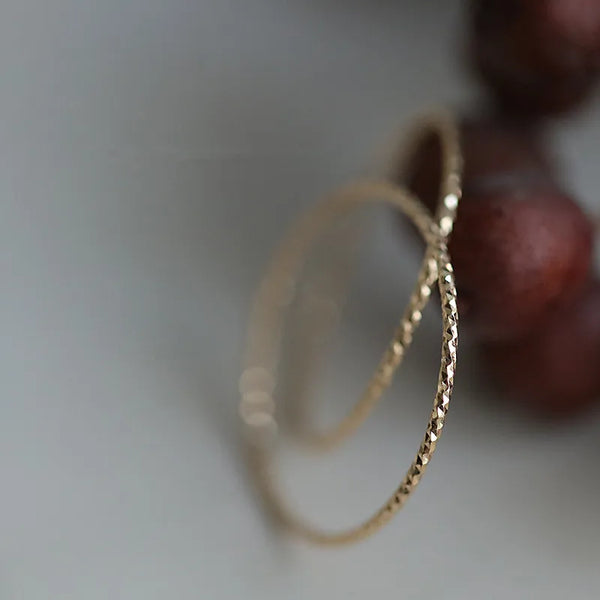 Primer plano de un anillo minimalista dorado con banda texturizada sobre una superficie oscura desenfocada.