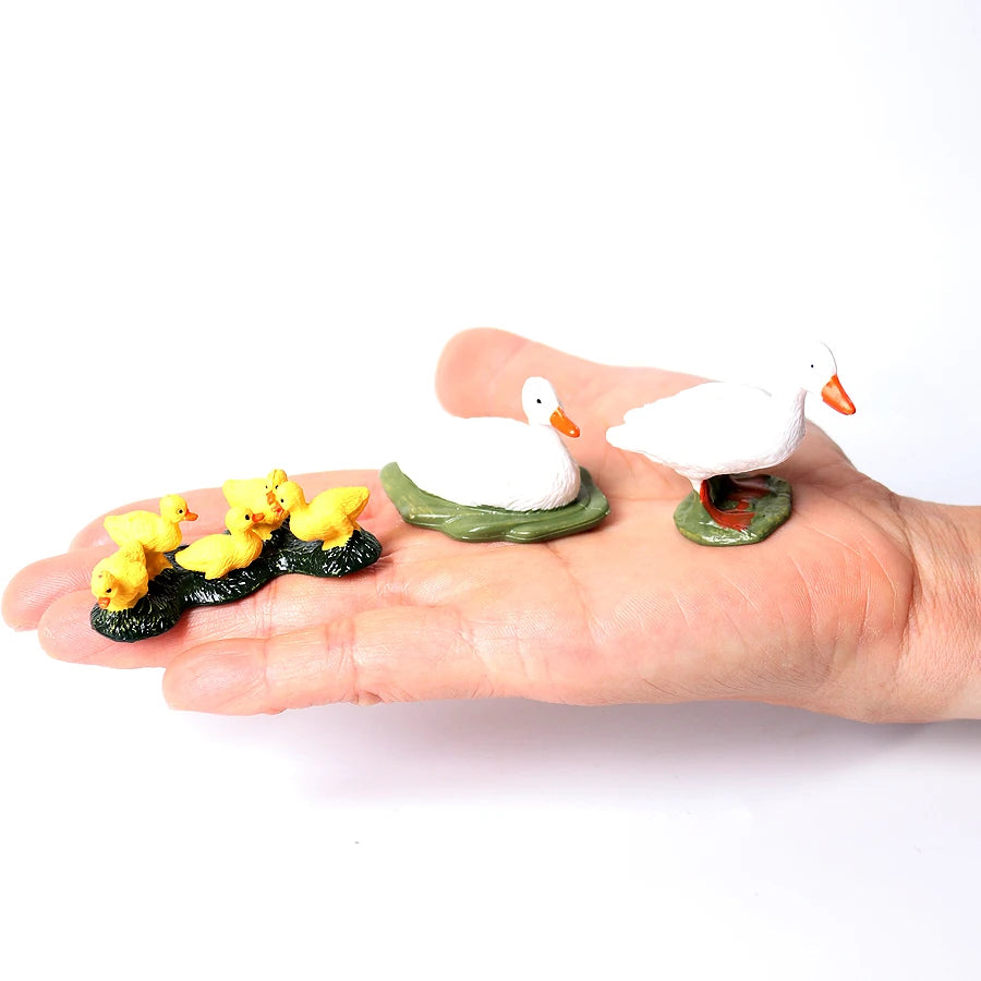 A hand holds several realistic animal figurines, including a white goose and yellow chicks, on a white background.