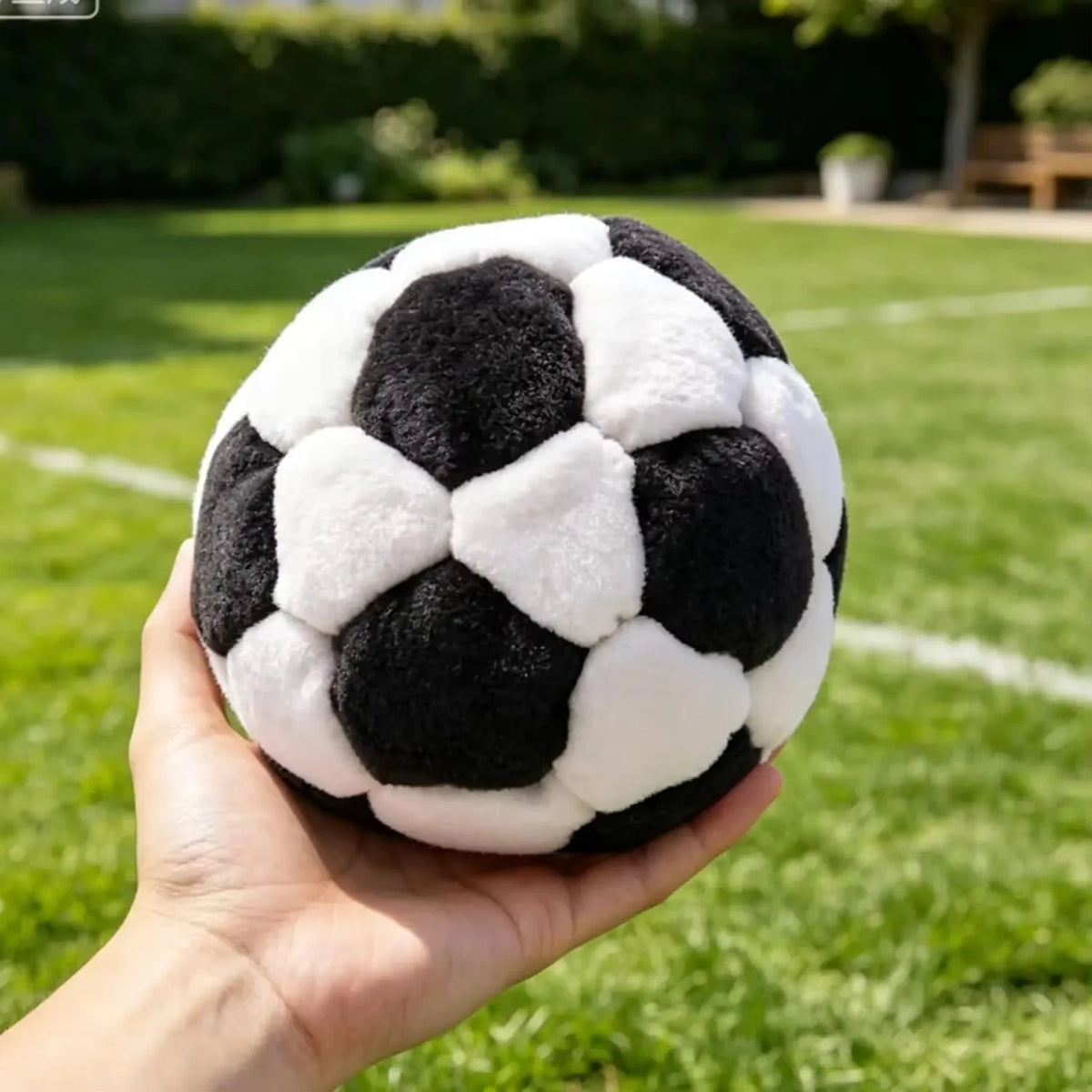 Un ballon de soccer crochet fait main avec texture douce noir et blanc tenu dans une main sur une pelouse verte.