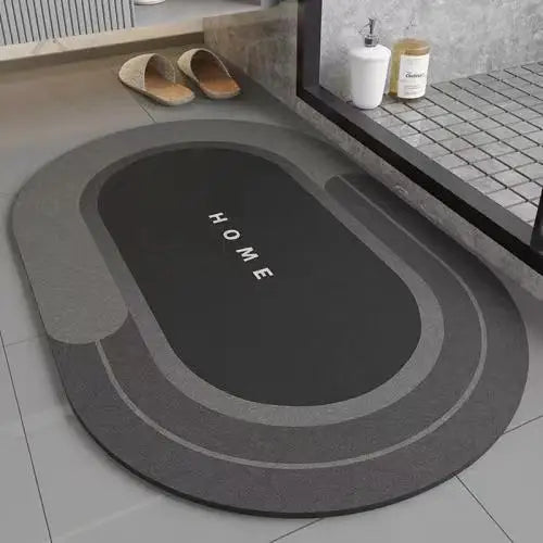 A round gray bath mat with a dark oval design and non-slip rubber base is displayed on a tiled floor.
