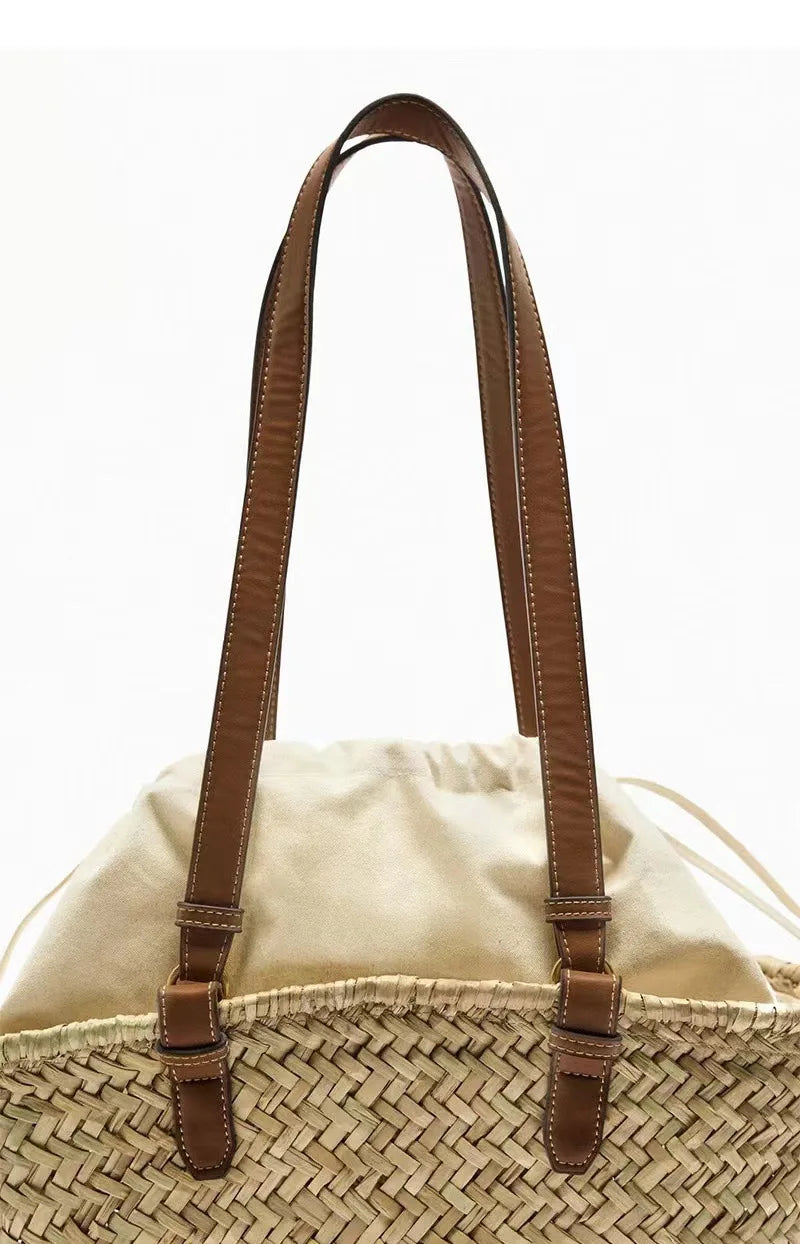 A close-up of a tan leather handle attached to a handwoven straw tote bag.