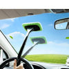 A hand is using a windshield cleaning brush with a green microfiber pad to clean a car's windshield.