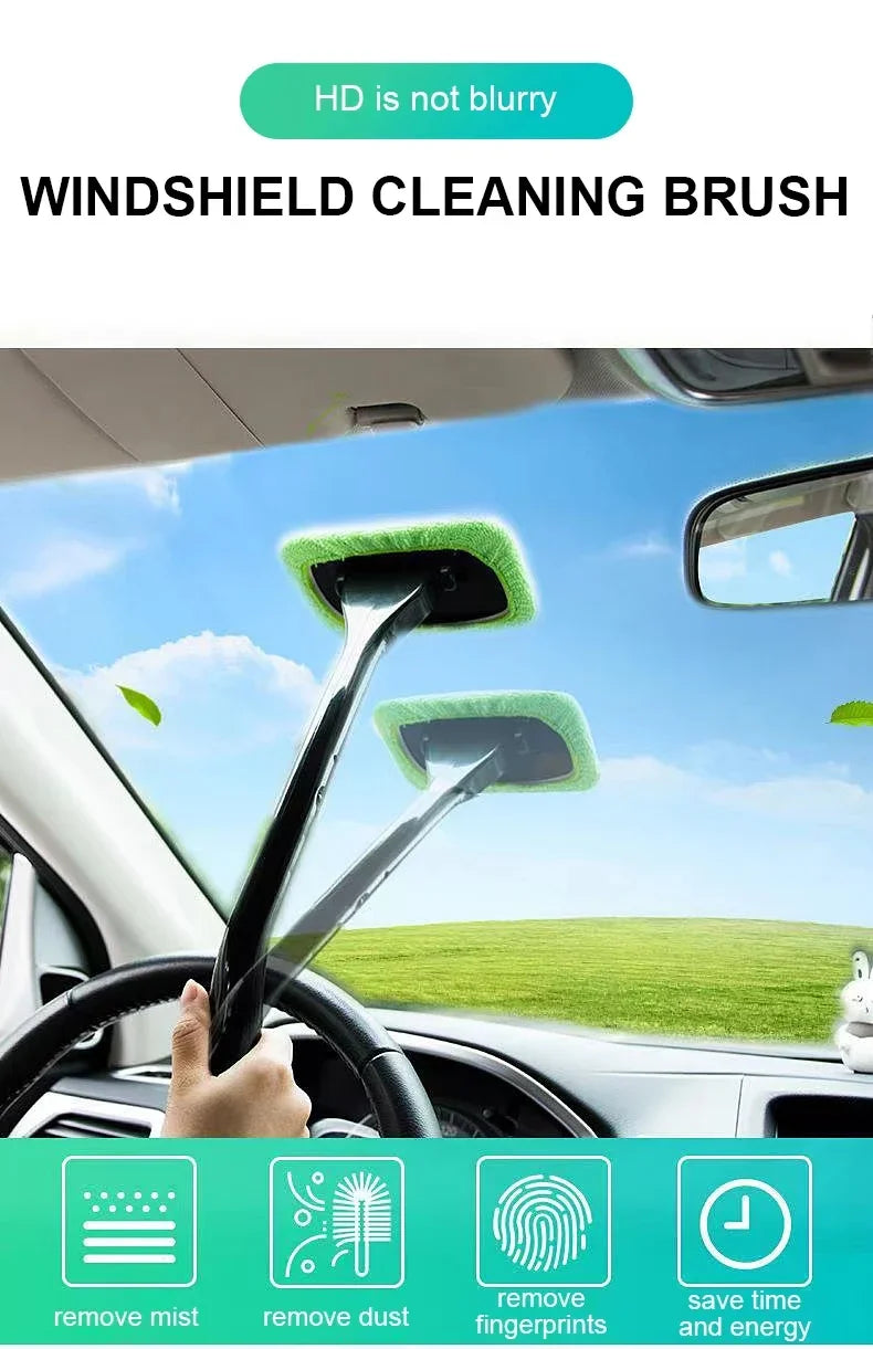 A hand is using a windshield cleaning brush with a green microfiber pad to clean a car's windshield.