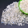 A pile of clear and translucent natural crystal stone chips in various sizes, some contained in a green bowl.