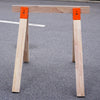 A wooden workbench top supported by heavy-duty orange steel brackets on an asphalt surface.