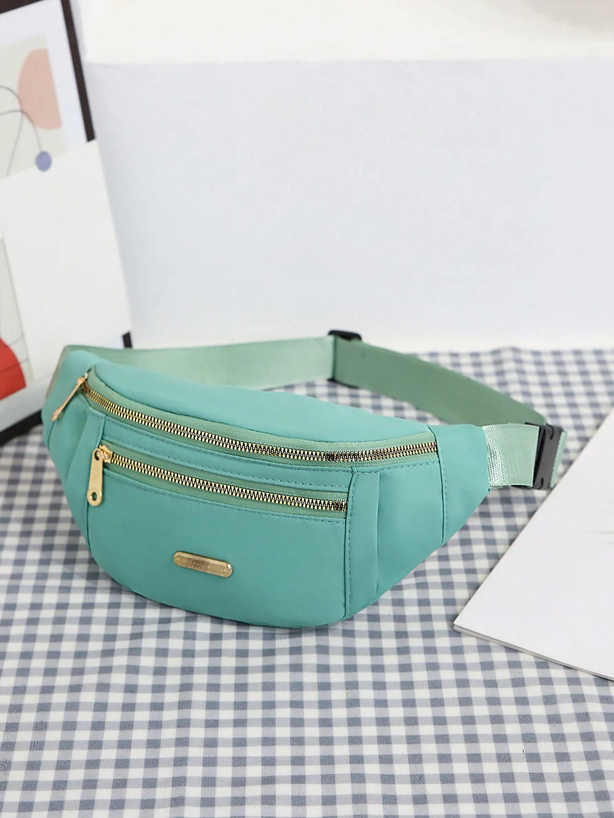 Mintgrüne Damen-Sport-Geldertasche mit Reißverschluss und goldenen Beschlägen auf karierter Oberfläche.