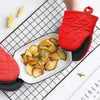 Red heat-resistant silicone oven mitts with black grips holding roasted potatoes on a white plate.