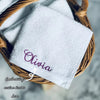 White embroidered face towel with the name Olivia in purple thread resting in a woven basket