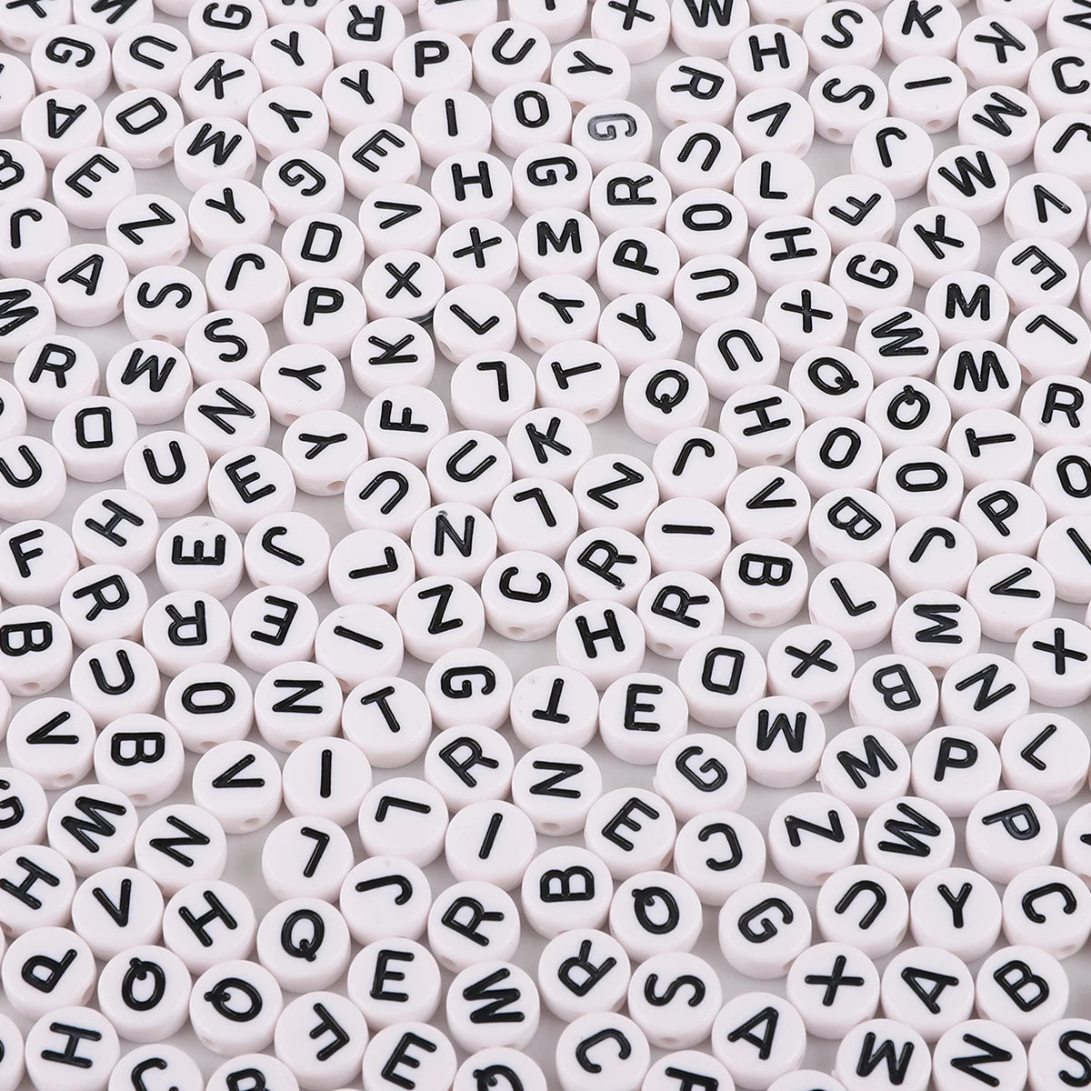 A close-up view of numerous white acrylic alphabet letter beads scattered on a surface.