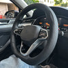A close-up view of a black steering wheel with a leather cover, showing the airbag and controls inside a car interior.