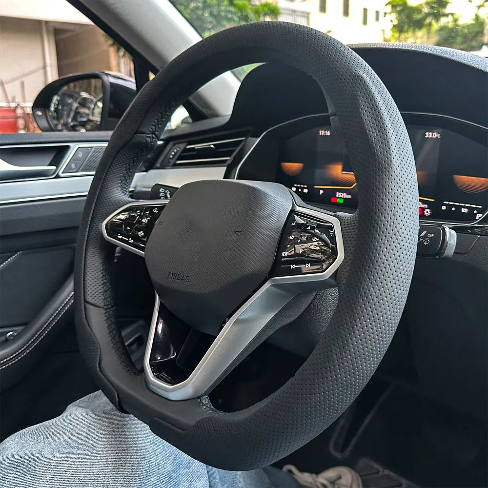 A close-up view of a black steering wheel with a leather cover, showing the airbag and controls inside a car interior.