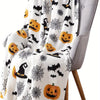 A white flannel throw blanket featuring a spooky Halloween print with black bats, spiders, and pumpkins draped over a gray ch