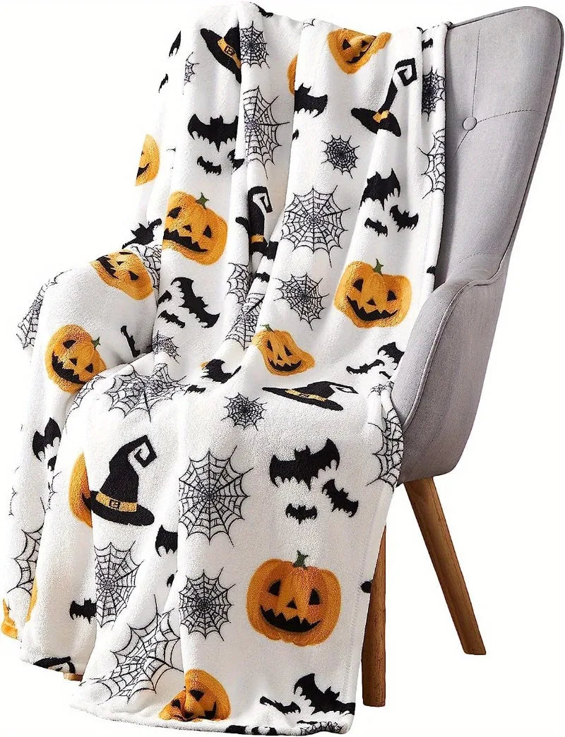 A white flannel throw blanket featuring a spooky Halloween print with black bats, spiders, and pumpkins draped over a gray ch