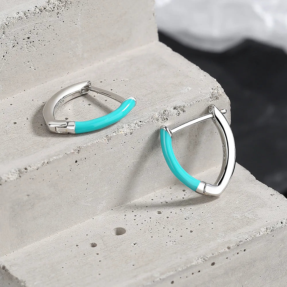 A pair of 925 sterling silver turquoise hoop earrings displayed on a light concrete surface.