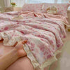 A pink floral washed cotton gauze summer quilt draped over a bed, with a hand touching the fabric.