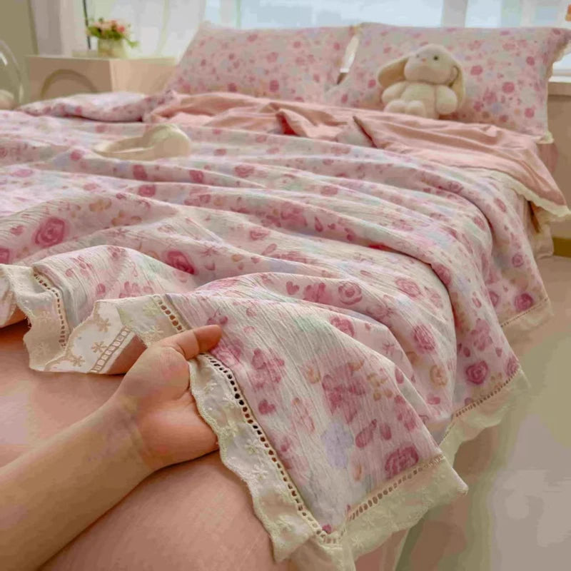 A pink floral washed cotton gauze summer quilt draped over a bed, with a hand touching the fabric.