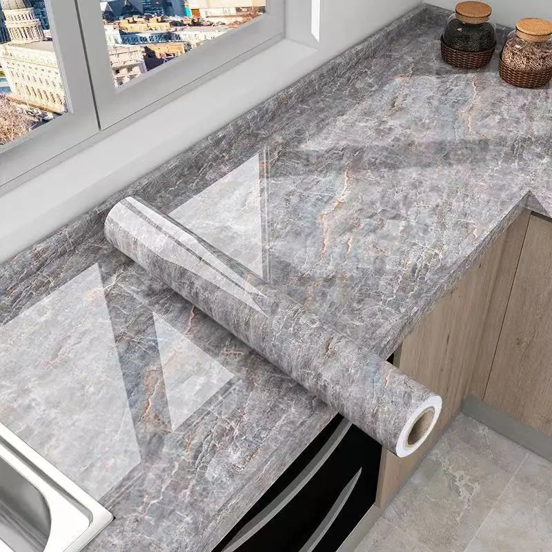 A slab of gray marble effect self-adhesive PVC film is displayed on a kitchen countertop next to cabinetry.