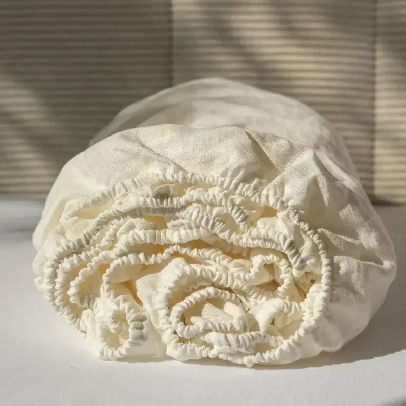 A rolled white linen fitted sheet with deep pockets resting on a white surface.
