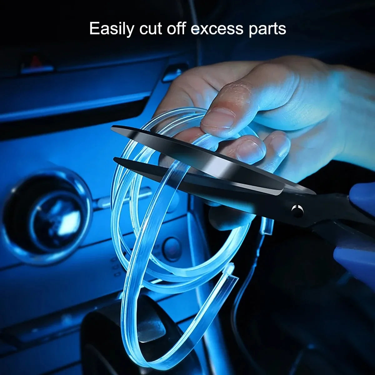 A hand uses a pair of scissors to cut excess parts of a flexible blue LED light strip inside a car interior.