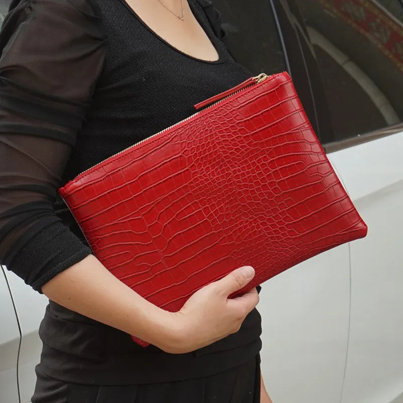 A woman holds a red crocodile-embossed PU leather envelope clutch against a black top.