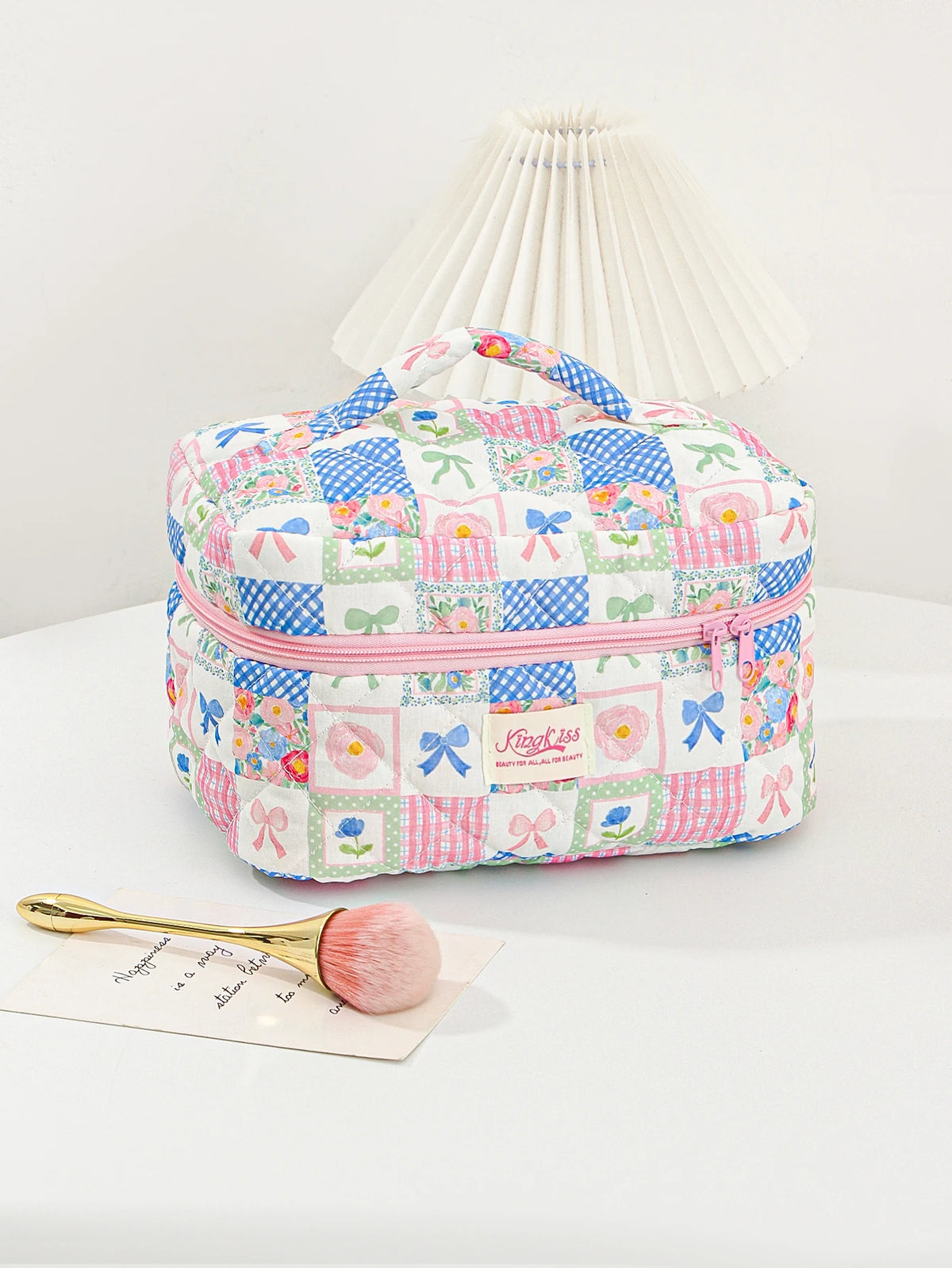 A pink and blue patchwork quilted makeup bag with a pleated lid rests on a white surface.