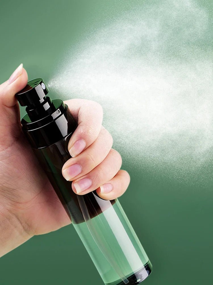 A hand is holding a dark glass spray bottle, releasing a fine mist of white powder against a green background.