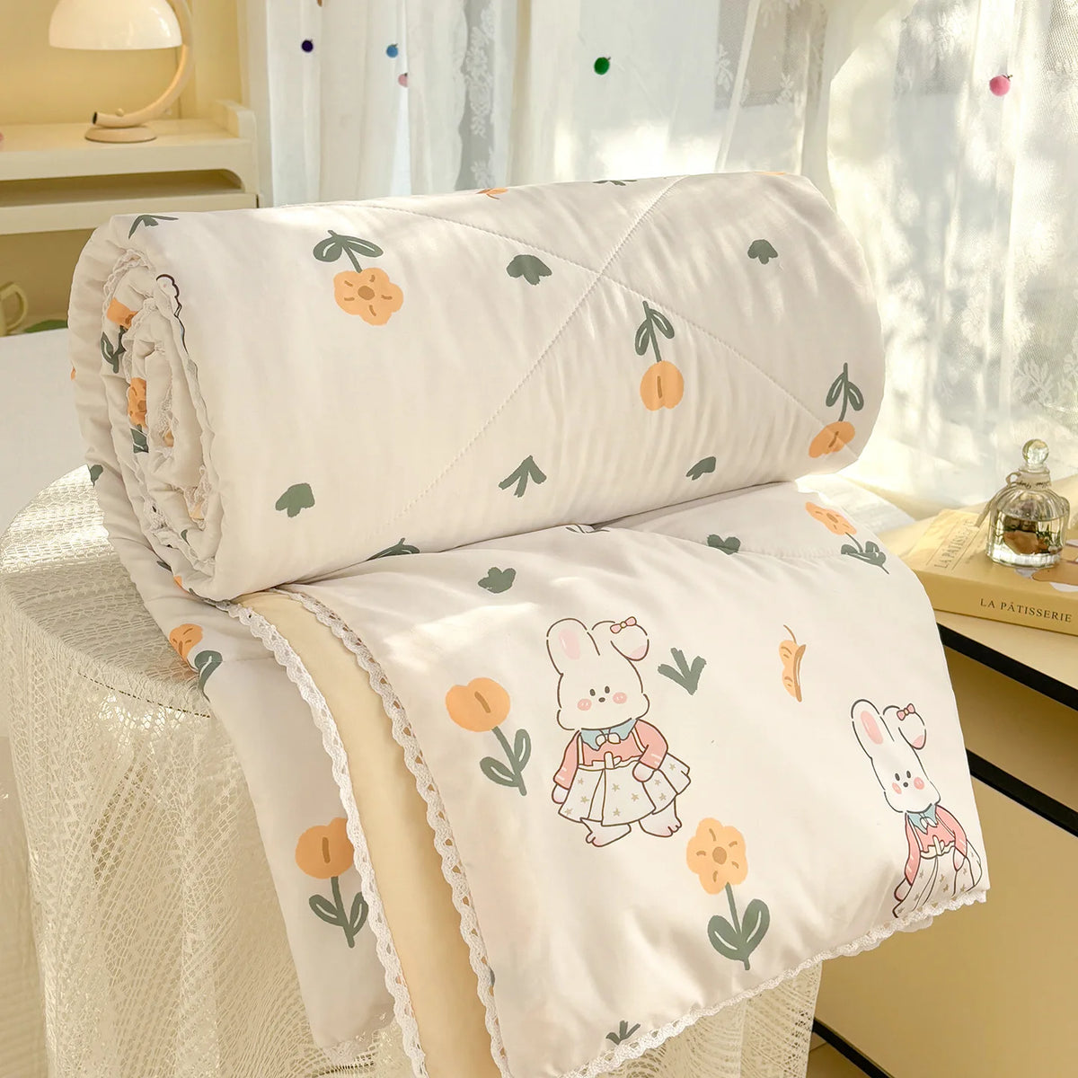 White comforter with a panda print featuring rabbits and flowers, folded on a white table.