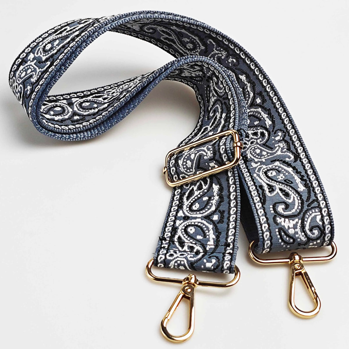 A navy blue and white paisley jacquard bag strap with gold hardware.