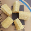 Five cylindrical natural loofah body scrubbers with hanging ropes arranged in a cross pattern.