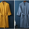 A mustard yellow waffle knit robe hanging on a wooden hanger against a dark blue wall.