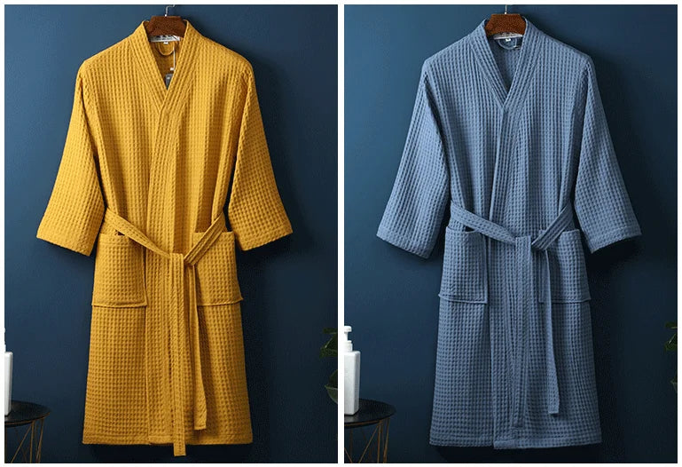 A mustard yellow waffle knit robe hanging on a wooden hanger against a dark blue wall.