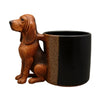 A brown dachshund figurine with a puppy handle sitting next to a black and tan coffee mug.