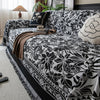 A black and white floral jacquard sofa blanket with tassels draped over a dark upholstered sofa.