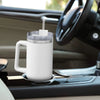 A white insulated stainless steel tumbler with a clear lid is placed on a car dashboard.