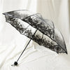 A black umbrella with a transparent canopy featuring a floral design, shown open against a white background.