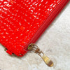 Close-up of a red crocodile embossed fabric bag with a gold metal zipper pull replacement slider.