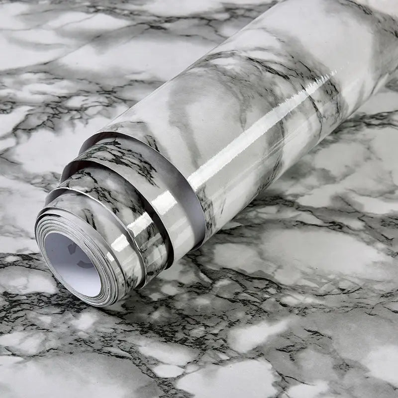 Roll of marble contact paper with gray and white veining lying on a marbled surface