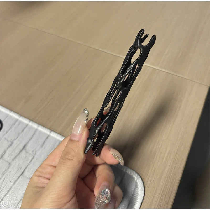 A hand holds a black willow wood wishing stick with intricate carvings against a light wooden background.