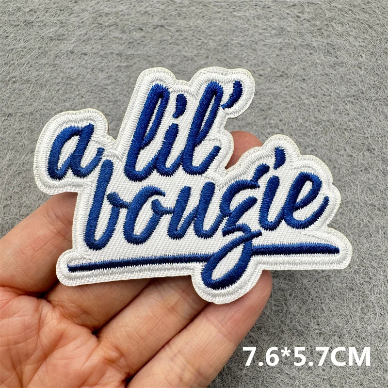 White and navy blue embroidered patch spelling out a lil bougie on a hand