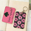 A pink and black patterned PU leather card holder with a flower design attached to a metal keyring.