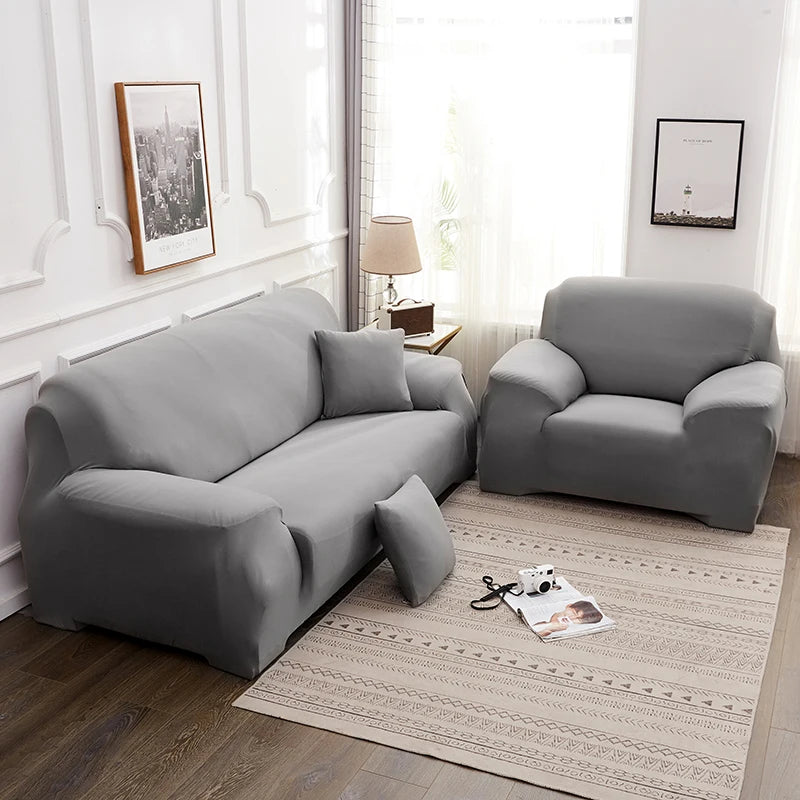 A modern gray stretchable sofa cover is displayed in a bright room with natural light.